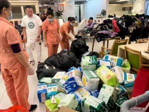 黃君俠 (P. Wong) 團隊捐贈大量尿布、成人紙尿褲及生活物資給養老院。工作人員正在清點和整理物資，展現社區關懷。