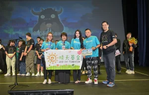 晴天基金代表、義工及黃君俠 P Wong 在童心同行慈善音樂晚會台上展示活動橫幅的合照。