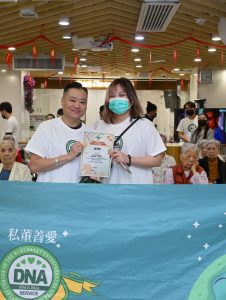 私董善愛《髮絲傳情・新年煥新》義剪活動現場，黃君俠與義工合照並展示感謝狀，推動長者關懷與社區公益行動。